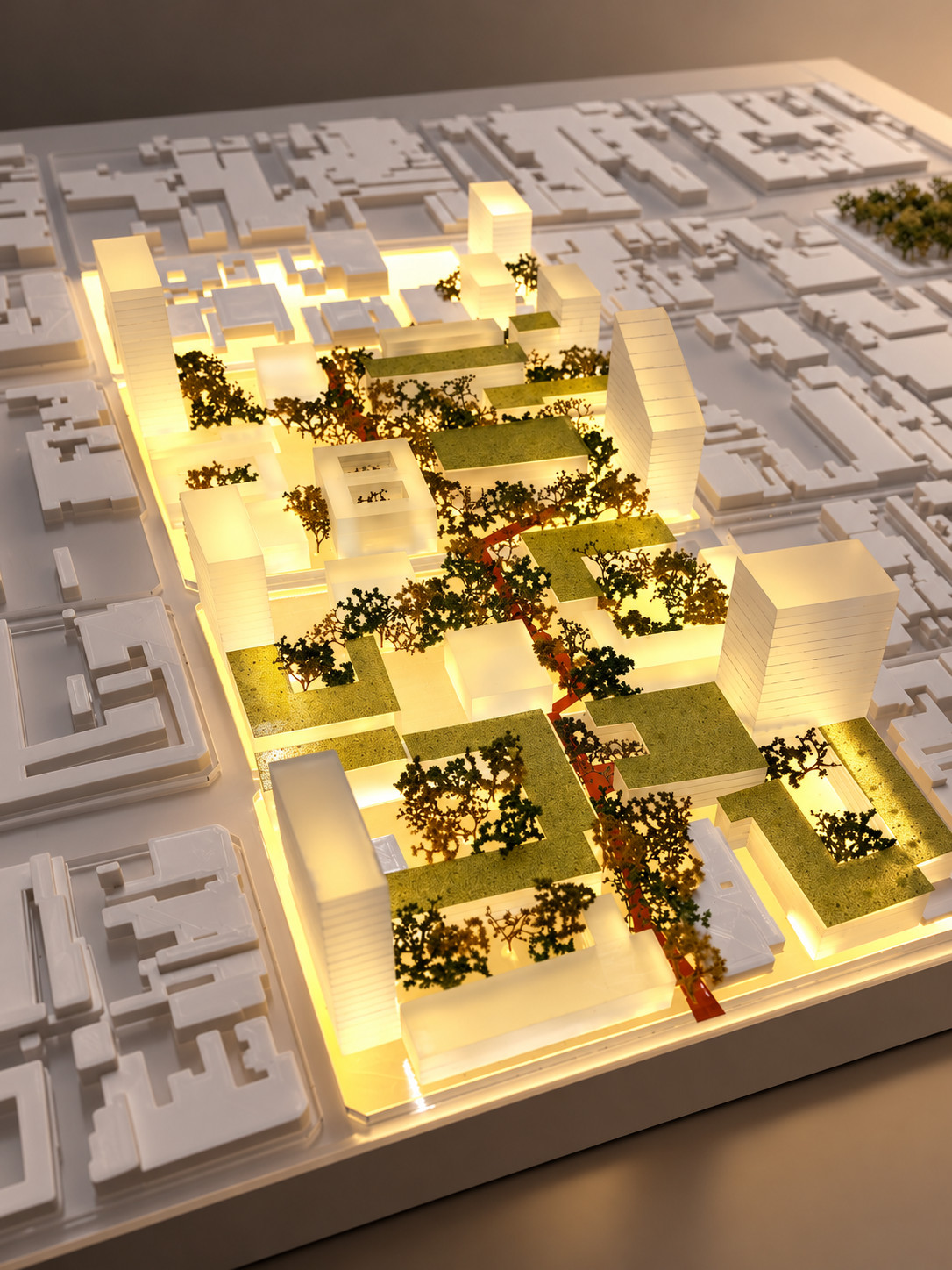 Maqueta urbana iluminada con vegetación, áreas verdes y un recorrido rojo, vista aérea